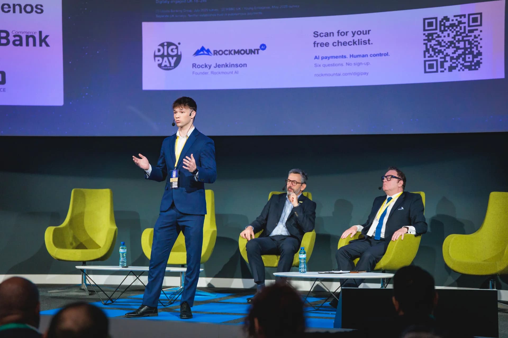 Rocky Jenkinson presenting on the DIGI PAY stage beside two seated conference speakers